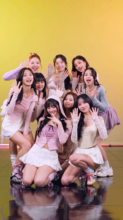 This contain TWICE posing for a photo in front of a yellow wall with their hands up