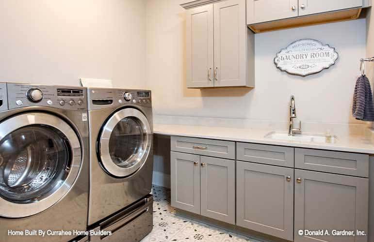 The laundry room is equipped with gray cabinets, a front-load washer and dryer, and a utility sink.