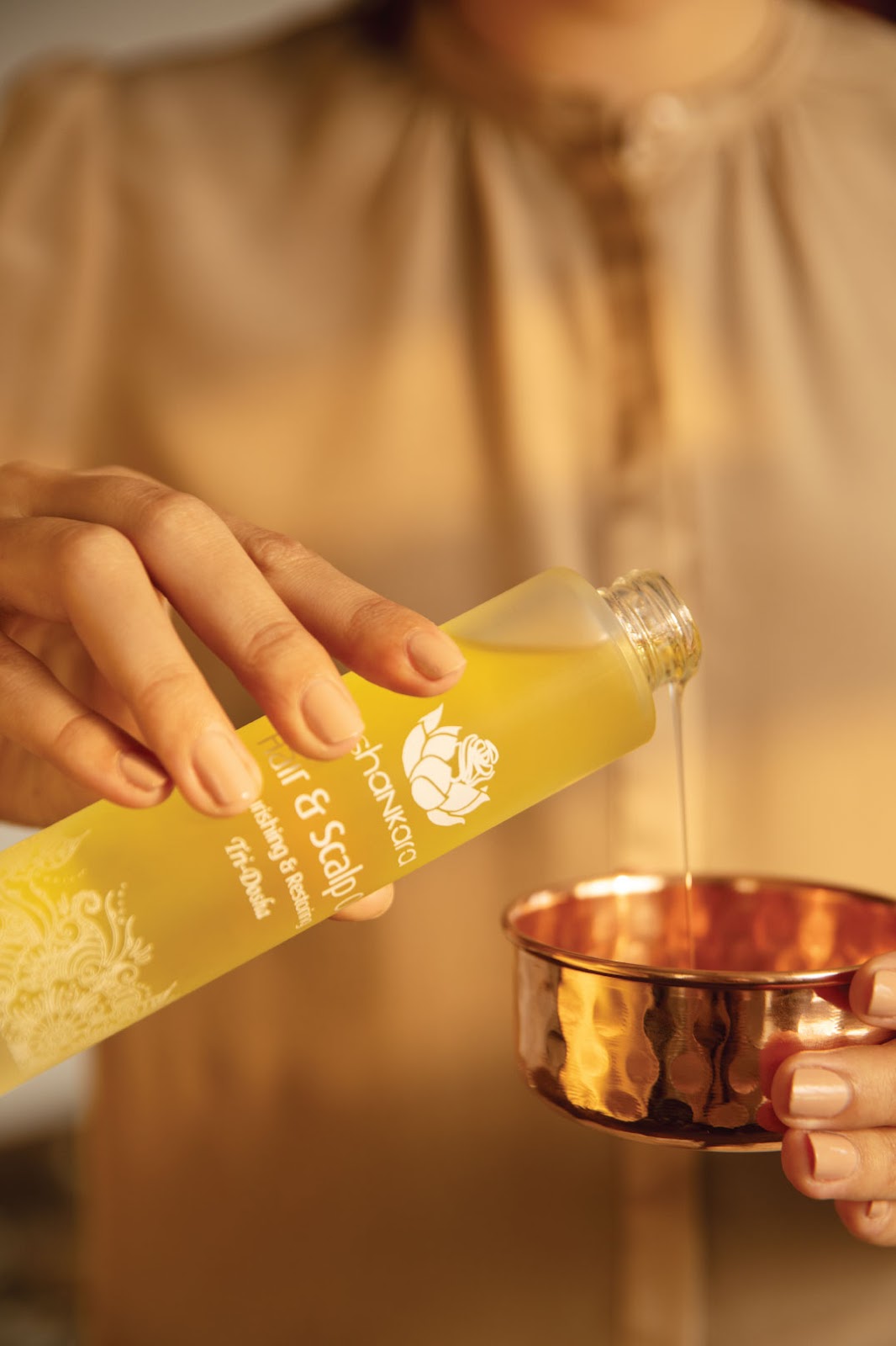 Woman pouring Shankara Natural Body Oil into golden bowl.Featured in the blog Luscious Locks: How Body Oil Can Transform Your Hair Care Routine