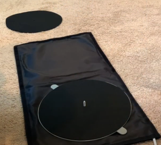 Turntable platter and mat placed on a soft black cover on a carpeted floor.