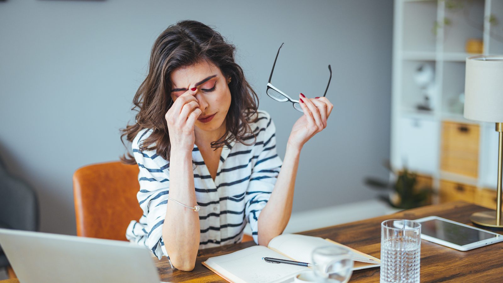 Seorang perempuan sedang kelelahan di depan laptop dan buku/Sumber: Canva