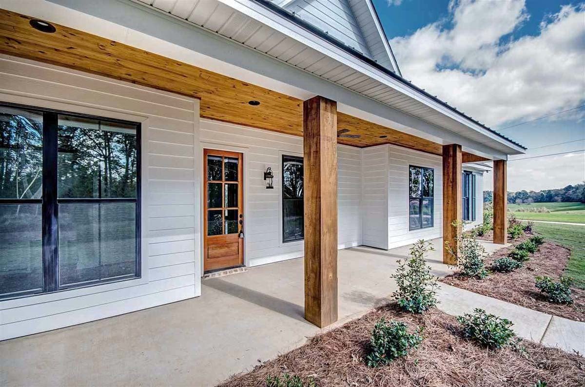Front covered porch with wooden posts and a glazed entry door fixed against the white siding.