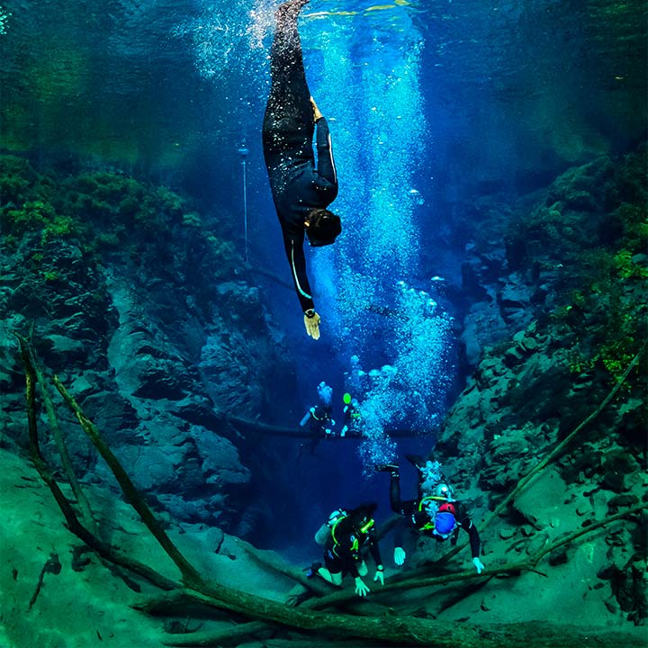 Mergulhadores explorando uma caverna subaquática com águas cristalinas e formação rochosa, praticando mergulho de cavernas em uma aventura emocionante.