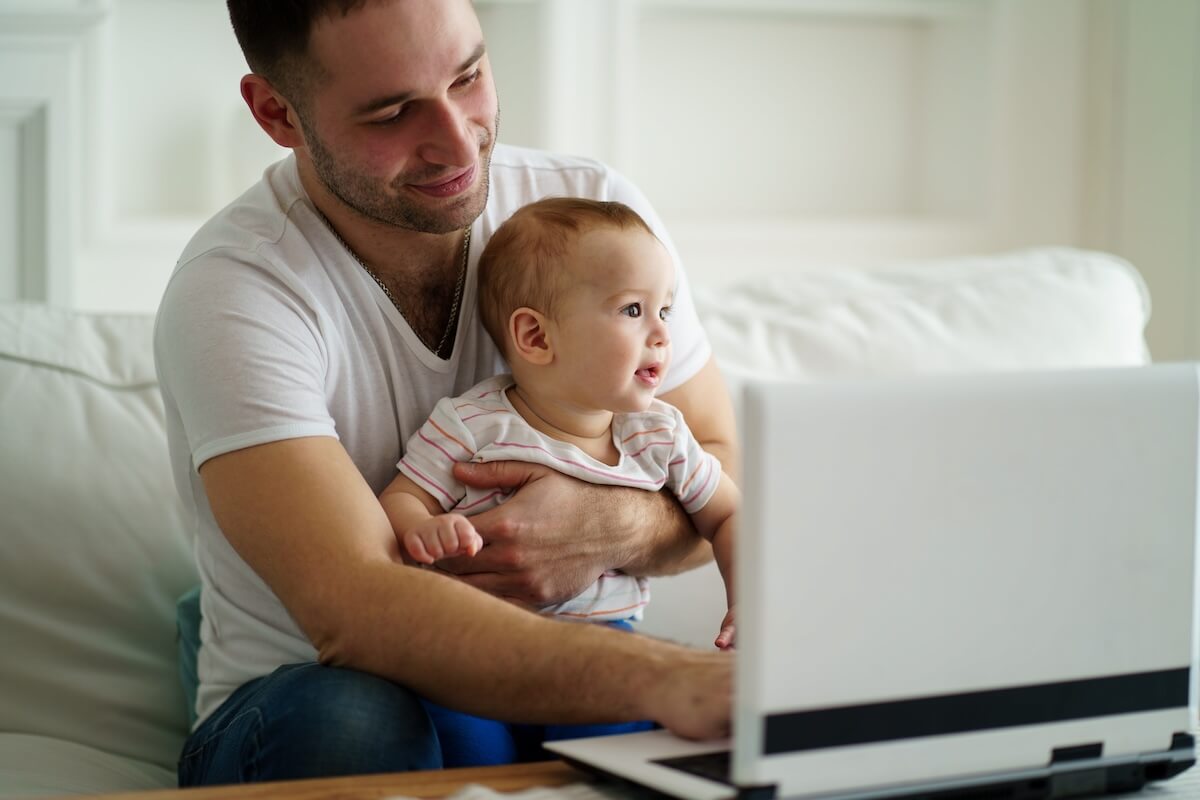 Employee benefits management: father taking care of his baby while using a laptop