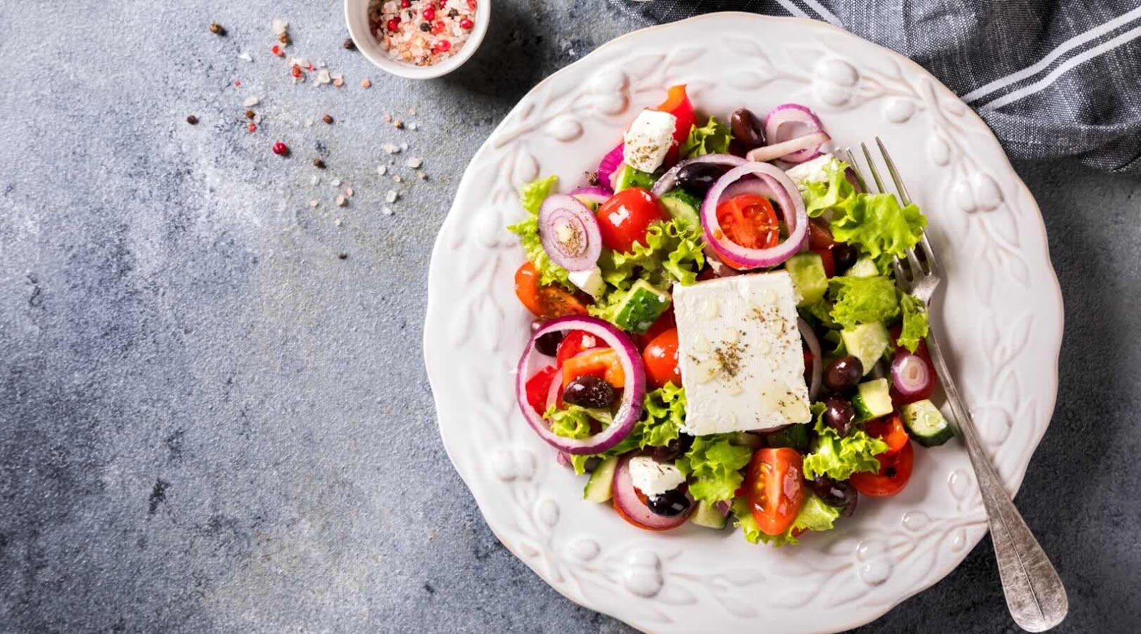 Fresh Greek salad featuring crisp lettuce, cherry tomatoes, cucumber, red onions, kalamata olives, and a block of feta cheese, drizzled with olive oil and sprinkled with herbs. This classic and healthy Mediterranean dish is a perfect choice for a nutritious meal, recommended by our registered dietitian in Mississauga.