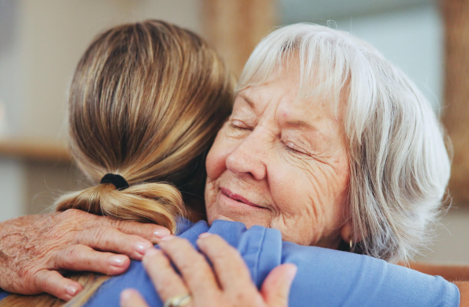 A close-up of a smiling older adult while they hug their caregiver in senior living.