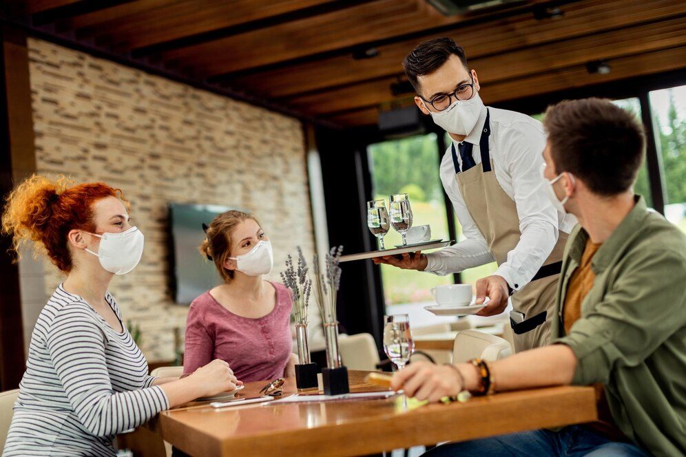 Three people wearing masks being served by a waiter wearing a mask.