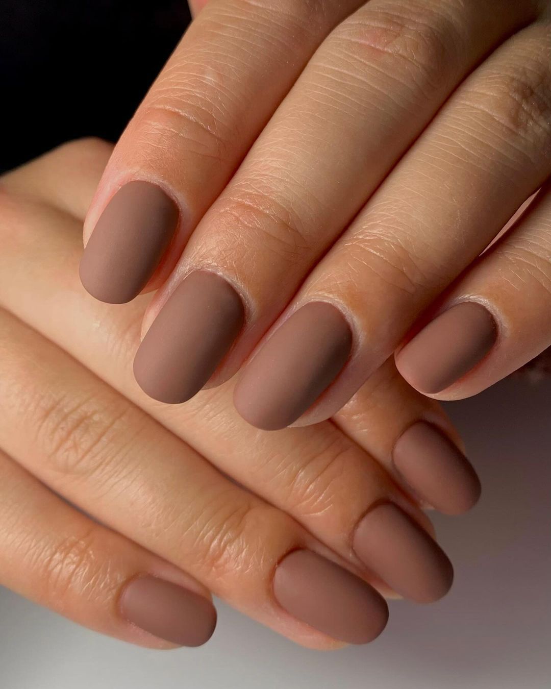 Close-up of a hand with matte brown manicured nails against a dark background.

