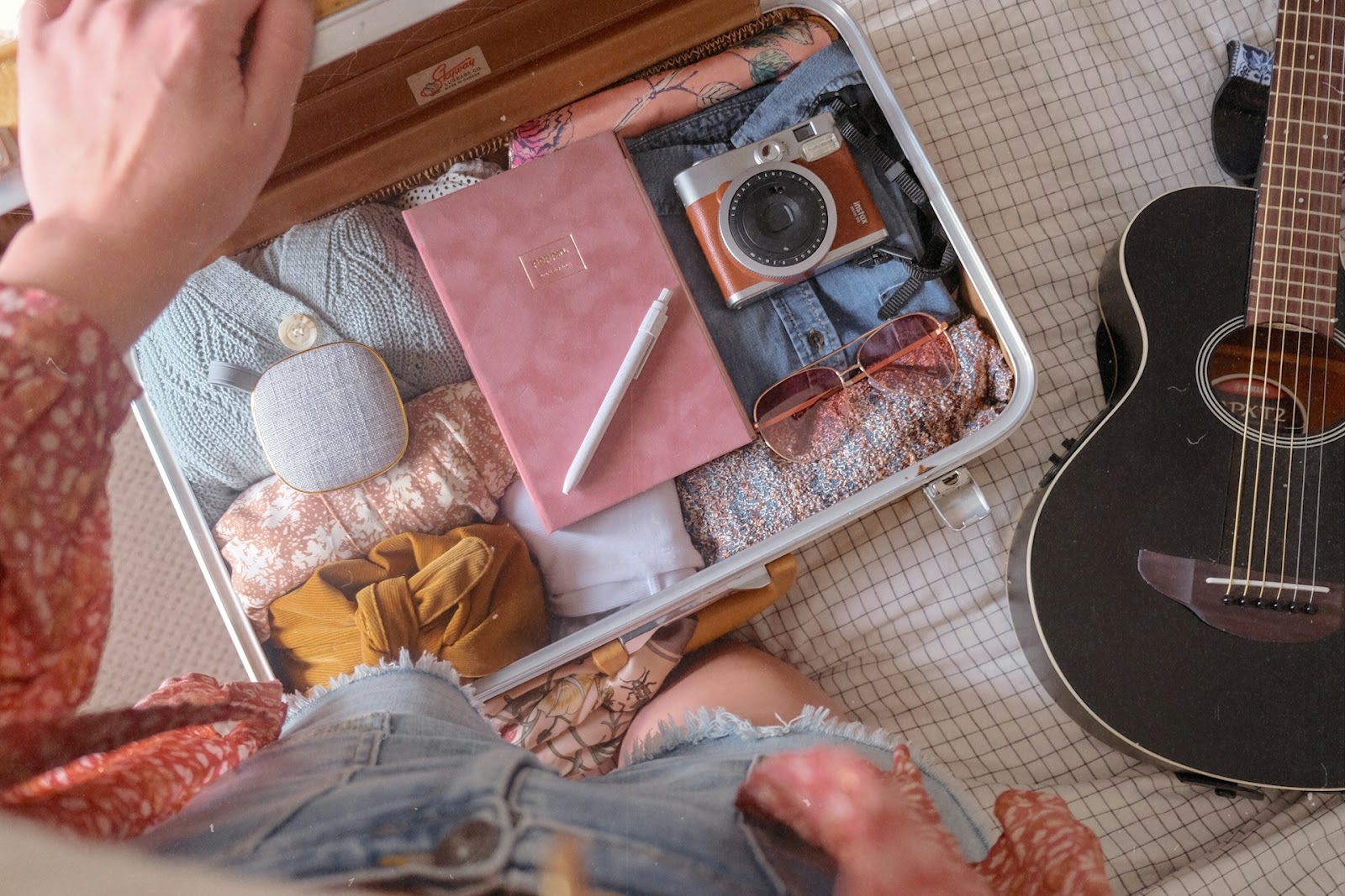 A person kneeling next to a suitcase with packed clothes next to a guitar.