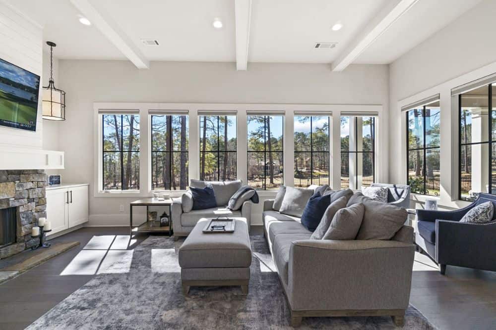 The keeping room features a beamed ceiling, gray seats, and a stone fireplace with a TV on top.