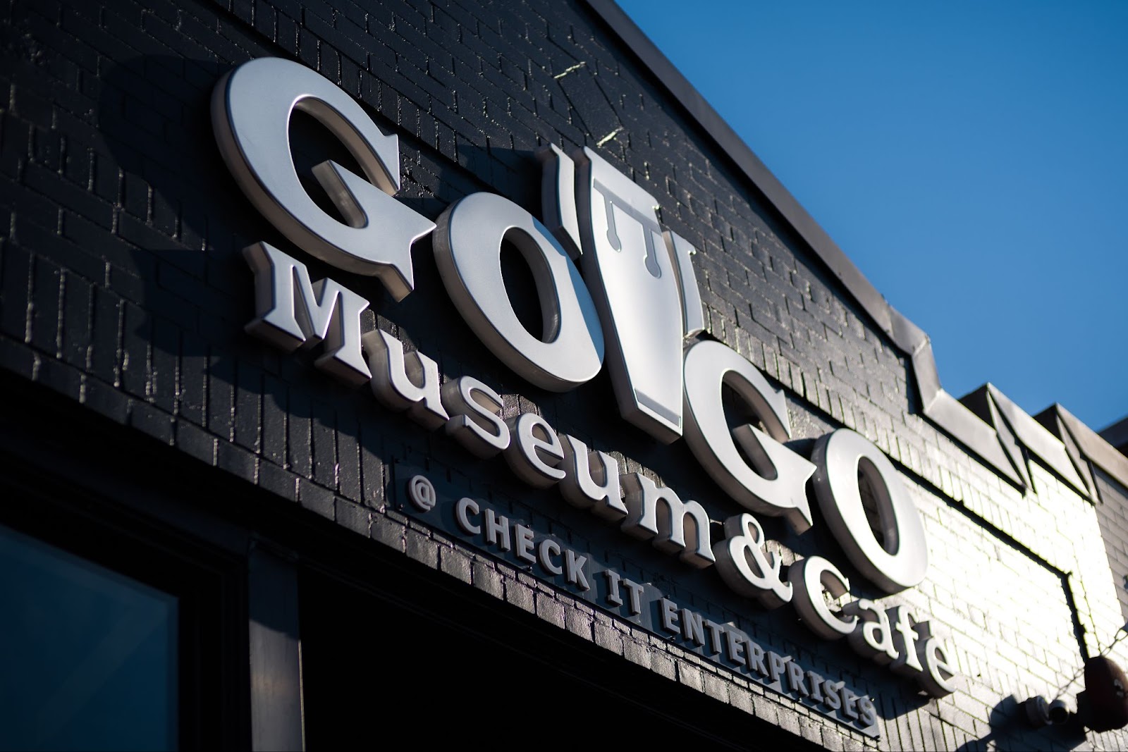 The outside of a black brick building that reads Go Go Museum & Cafe @ Check It Enterprises.