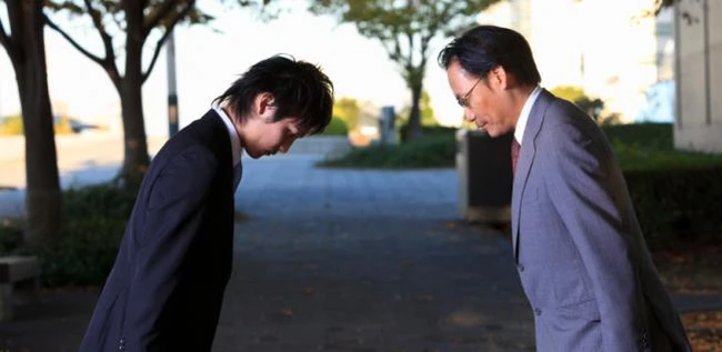 A Japanese man bowing lower than his boss.