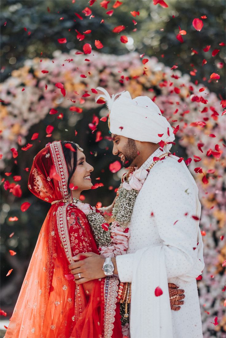 Indian wedding Varmala ceremony captured in a candid moment, with rose petals falling around the couple.