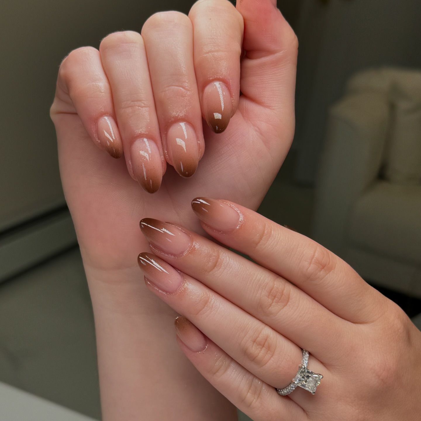 Close-up of hands with glossy taupe manicured nails and a sparkling butterfly ring on the finger.

