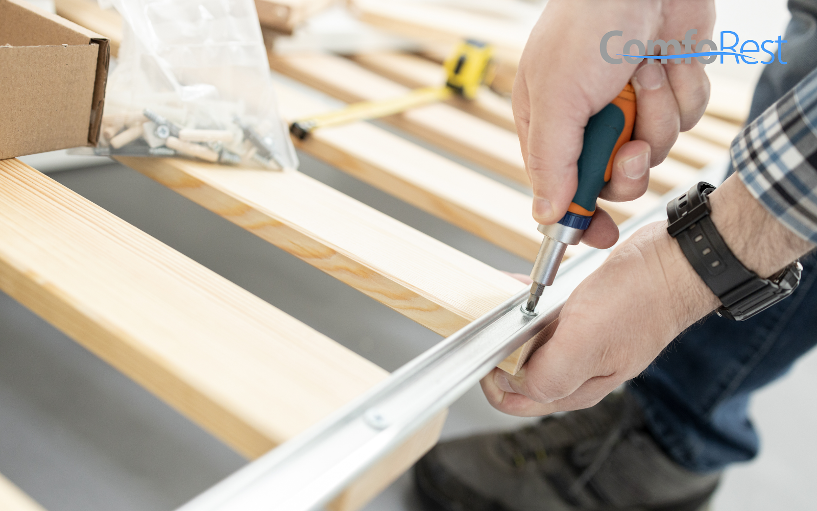 Person assembling a wooden slatted bed frame with a screwdriver.