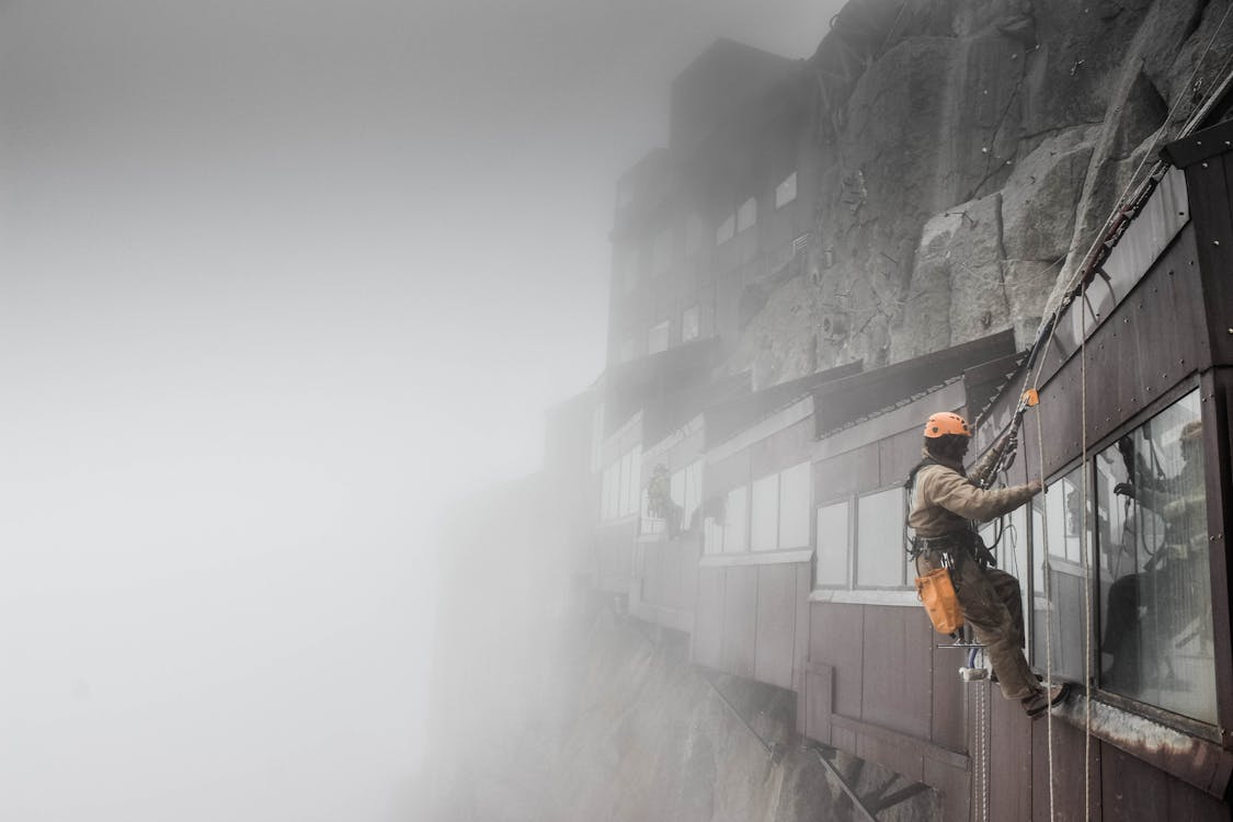 Worker using safety equipment on a high-rise building, illustrating operational risk management steps in hazardous environments.