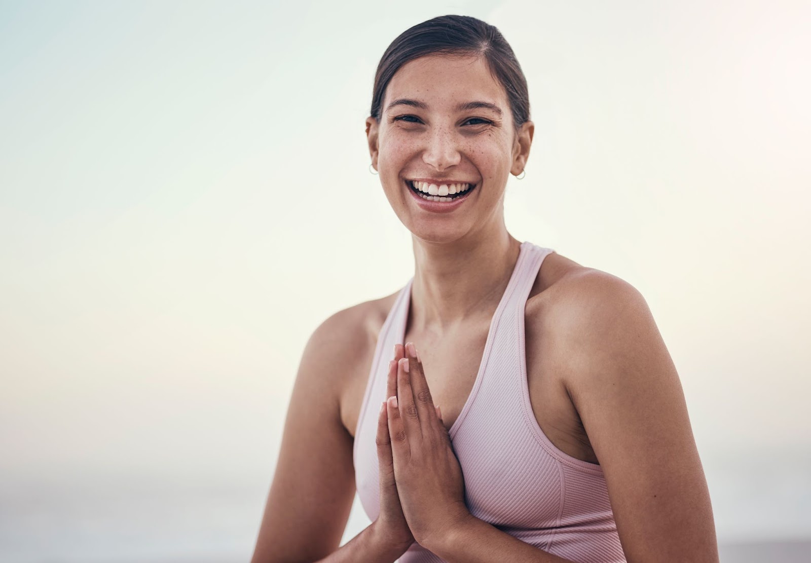 Woman with her hands pressed together and smiling outside. 