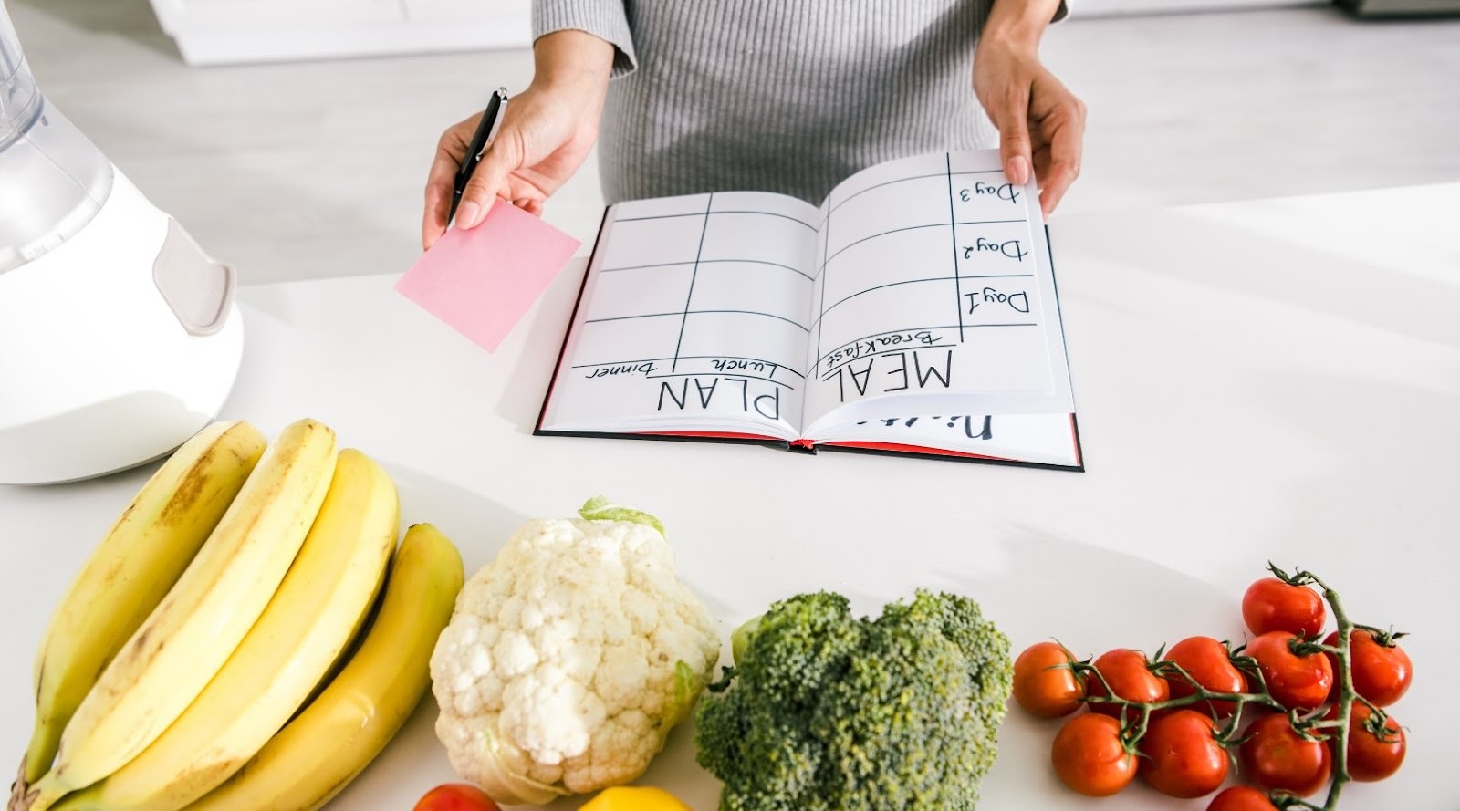 Cropped view of a woman meal planning with fruit and vegetables on the counter.