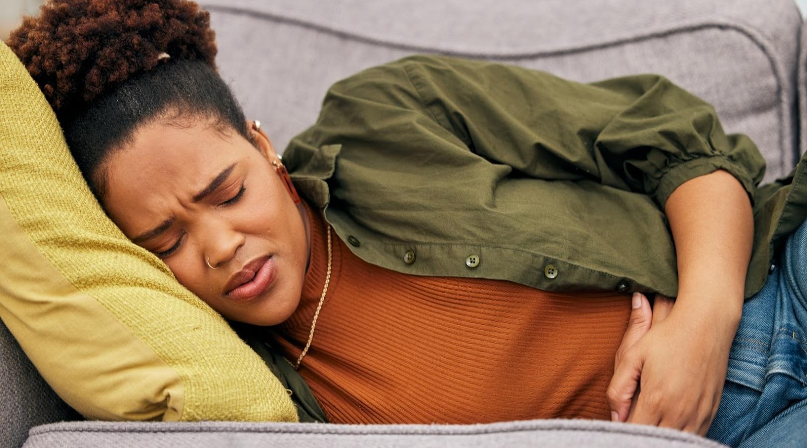 Woman lying on a couch holding her stomach in pain, with a pained expression on her face.