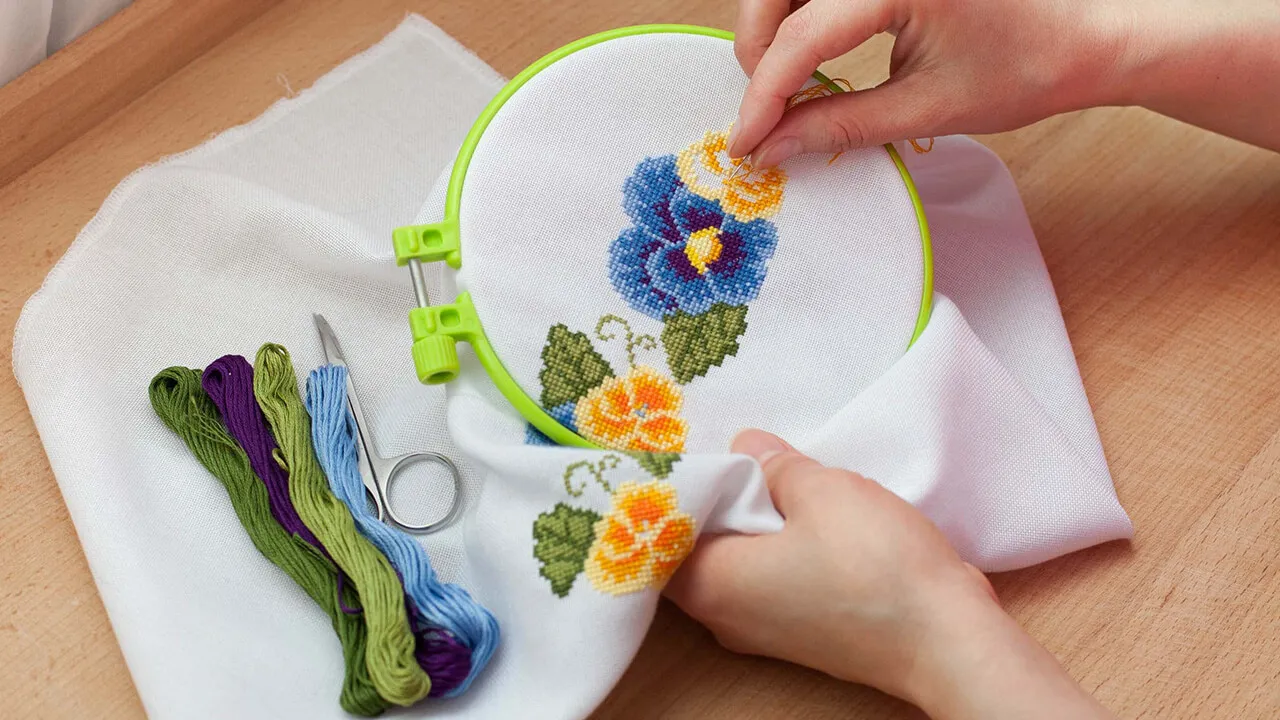 Close-up of embroidery hoop with colorful thread and detailed floral stitching, showcasing freestyle stitch art techniques
