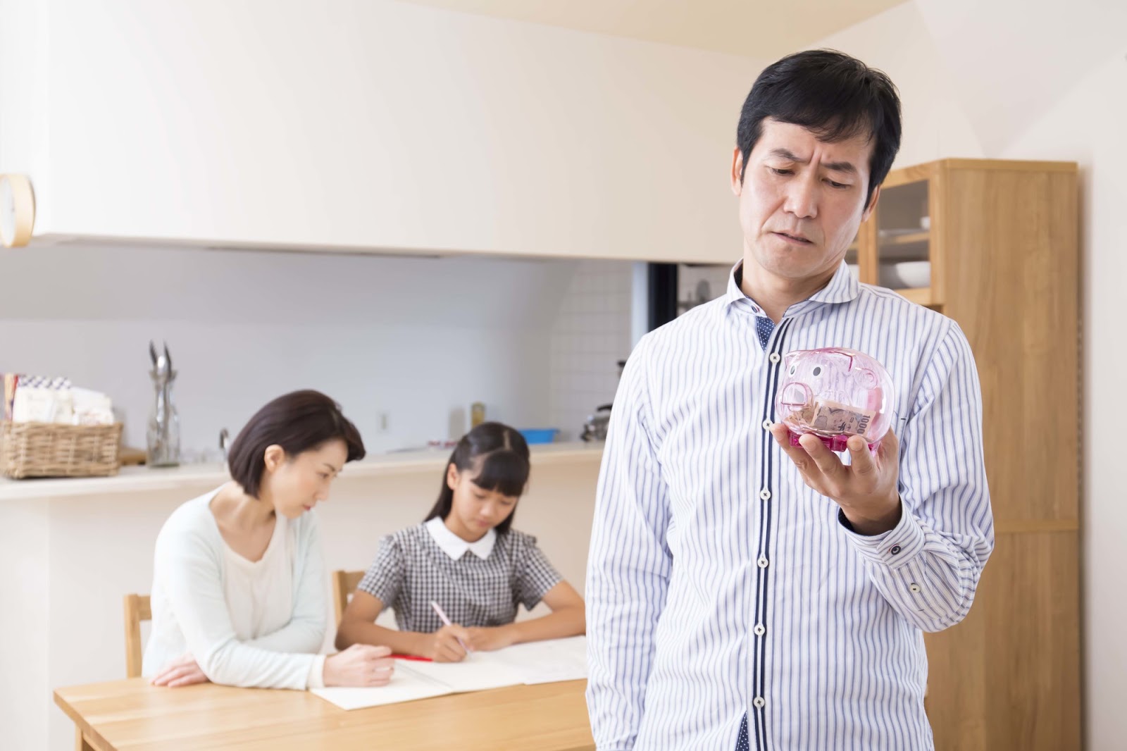 住宅ローンの返済に不安を感じる父親と家計を支える家族の様子（貯金箱を見つめる男性）