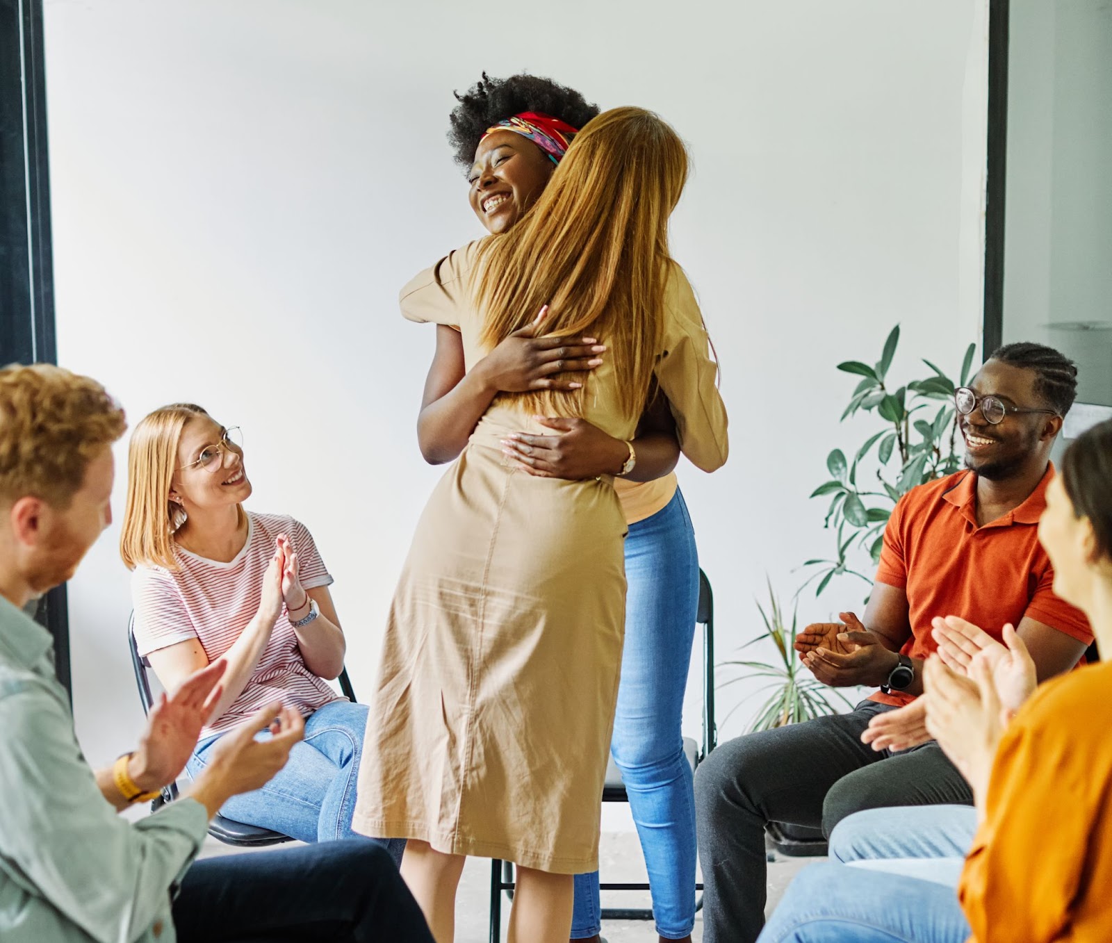 Two women hugging, people clapping, and sitting in a circle around them