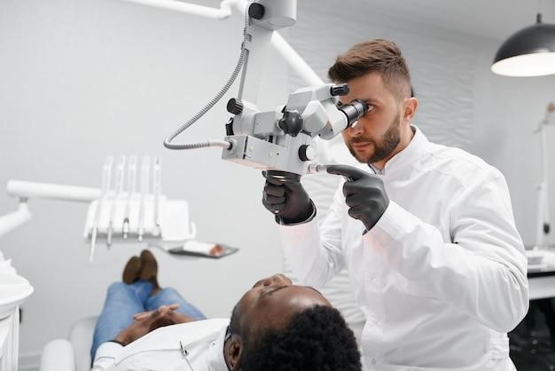 Male dentist examining teeth of male patient in clinic