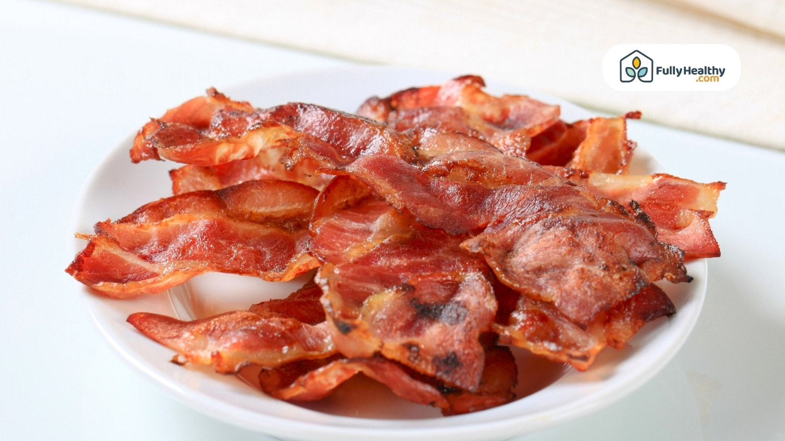 Crispy cooked bacon strips piled on white ceramic plate