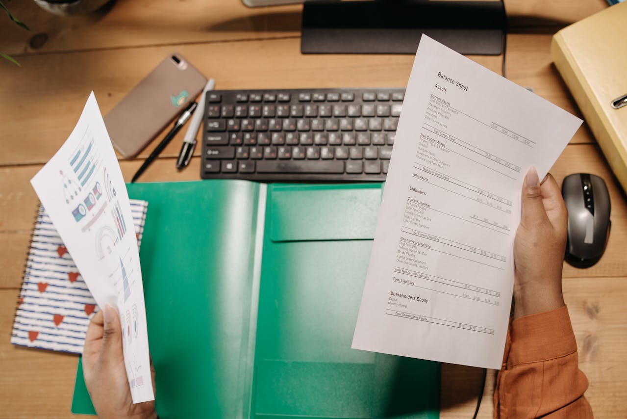  A person infront of a desktop, holding and analyzing a balance sheet 