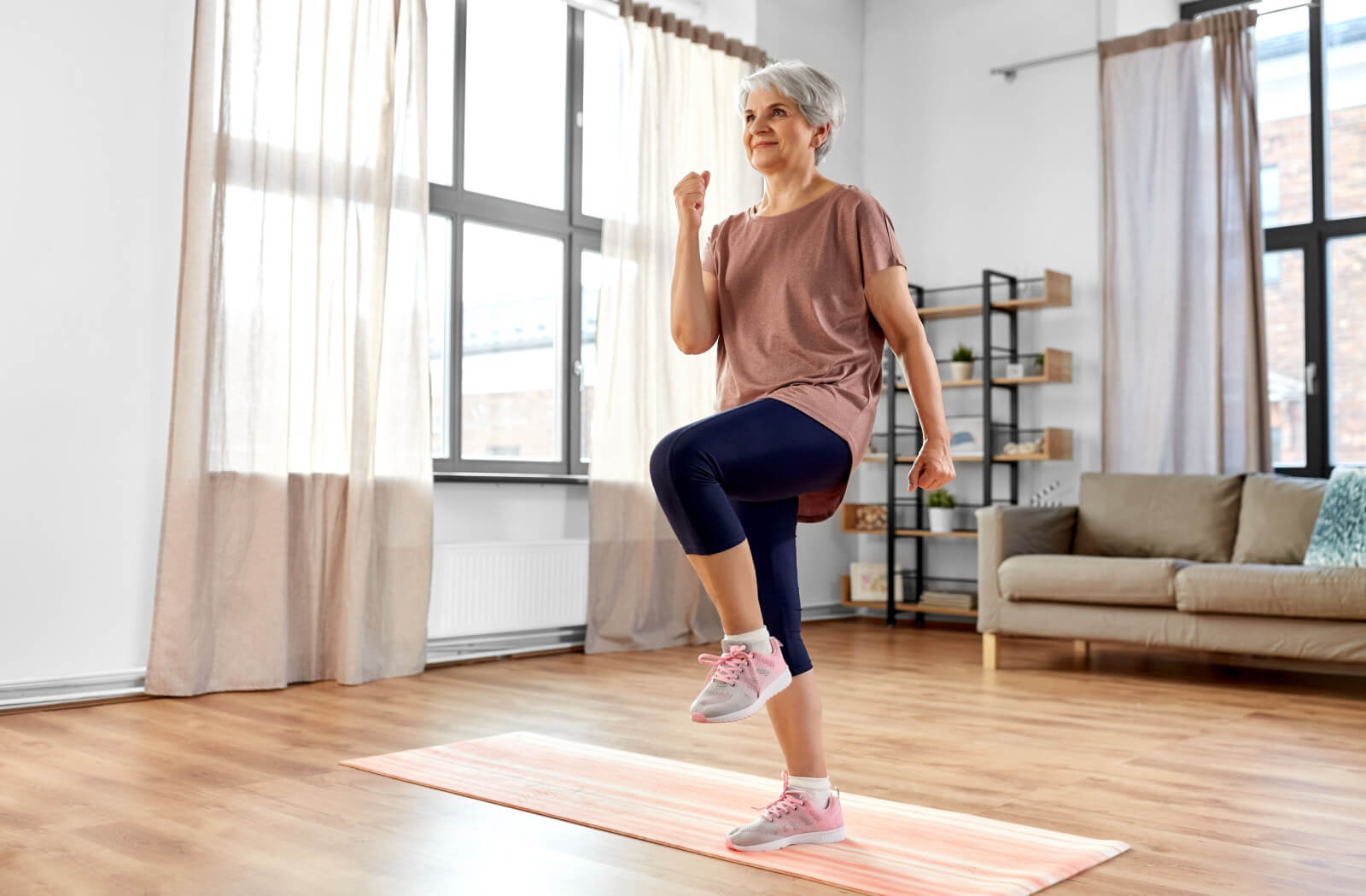 An older adult in an open living room marching in place as a leg strengthening exercise.