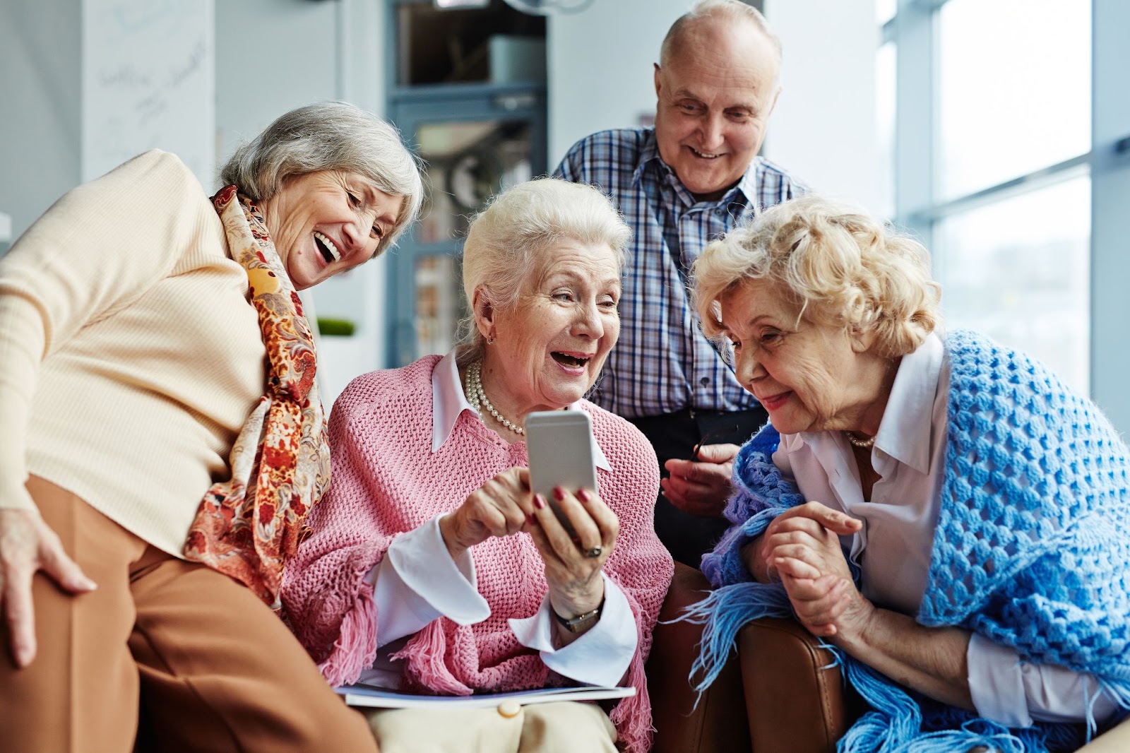 A smiling senior woman showing off her cell phone to her friends in senior living.