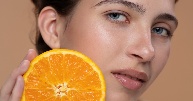 Close-up de uma mulher com uma laranja perto do rosto.