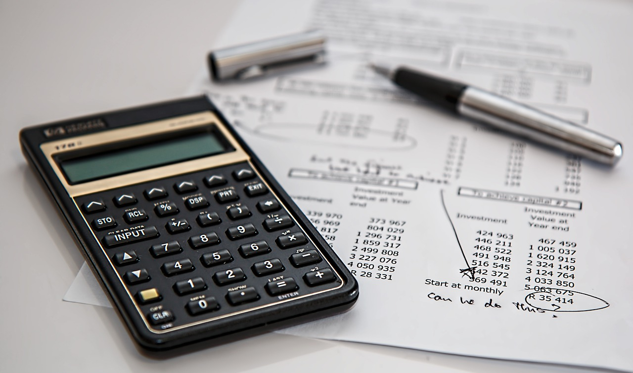 A calculator and pen placed on top of financial documents with handwritten notes and circled numbers