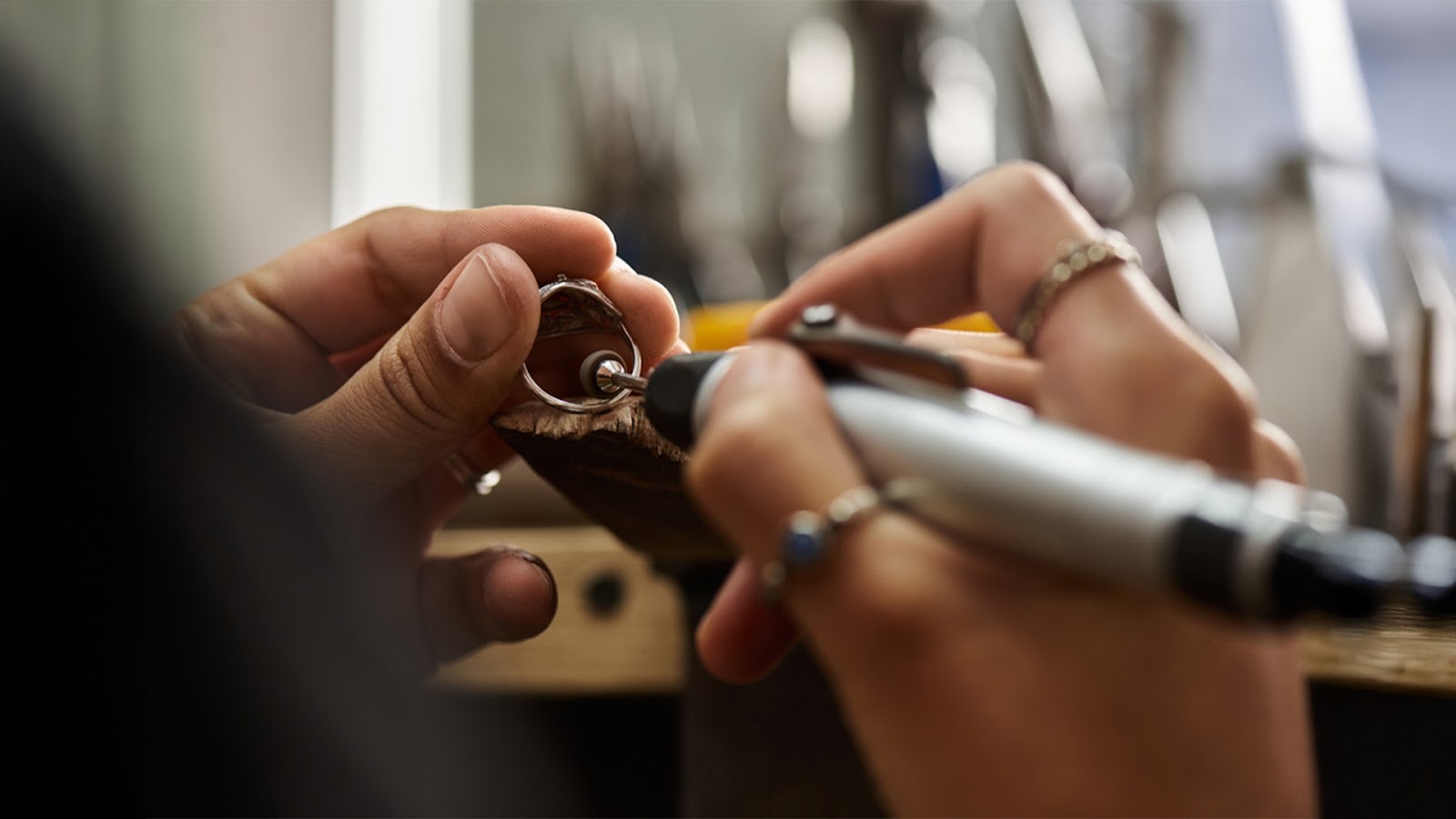A person is engaged in jewelry making, using a tool to refine a ring, showcasing skill and precision in their work.