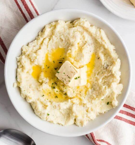 Garlic herb mashed potatoes with butter on top in a white bowl