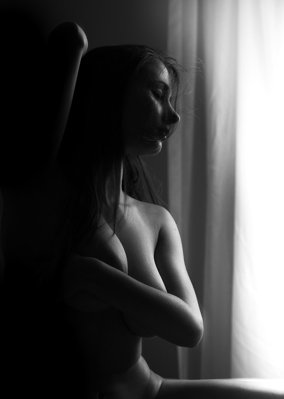 A photo of a nude woman sitting, with her left arm across her chest