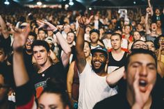 This contains an image of  a large group of people at a concert with their hands in the air and one person holding his head up