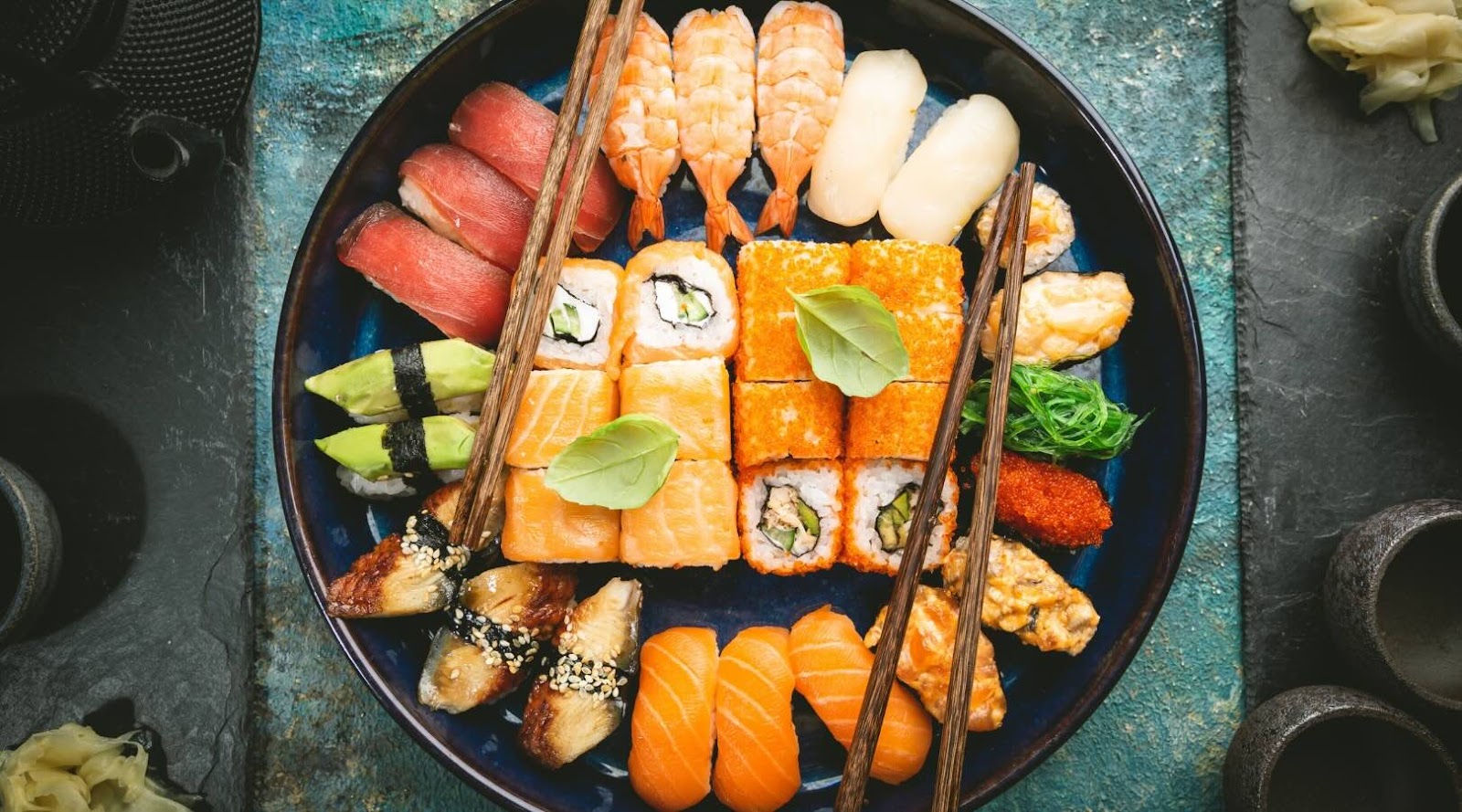 Colorful assortment of sushi and maki rolls featuring fresh tuna, salmon, shrimp, and avocado, arranged on a dark plate with chopsticks. This visually appealing and healthy Japanese dish is ideal for those seeking nutritious and delicious dining options in Mississauga, recommended by our registered dietitian.