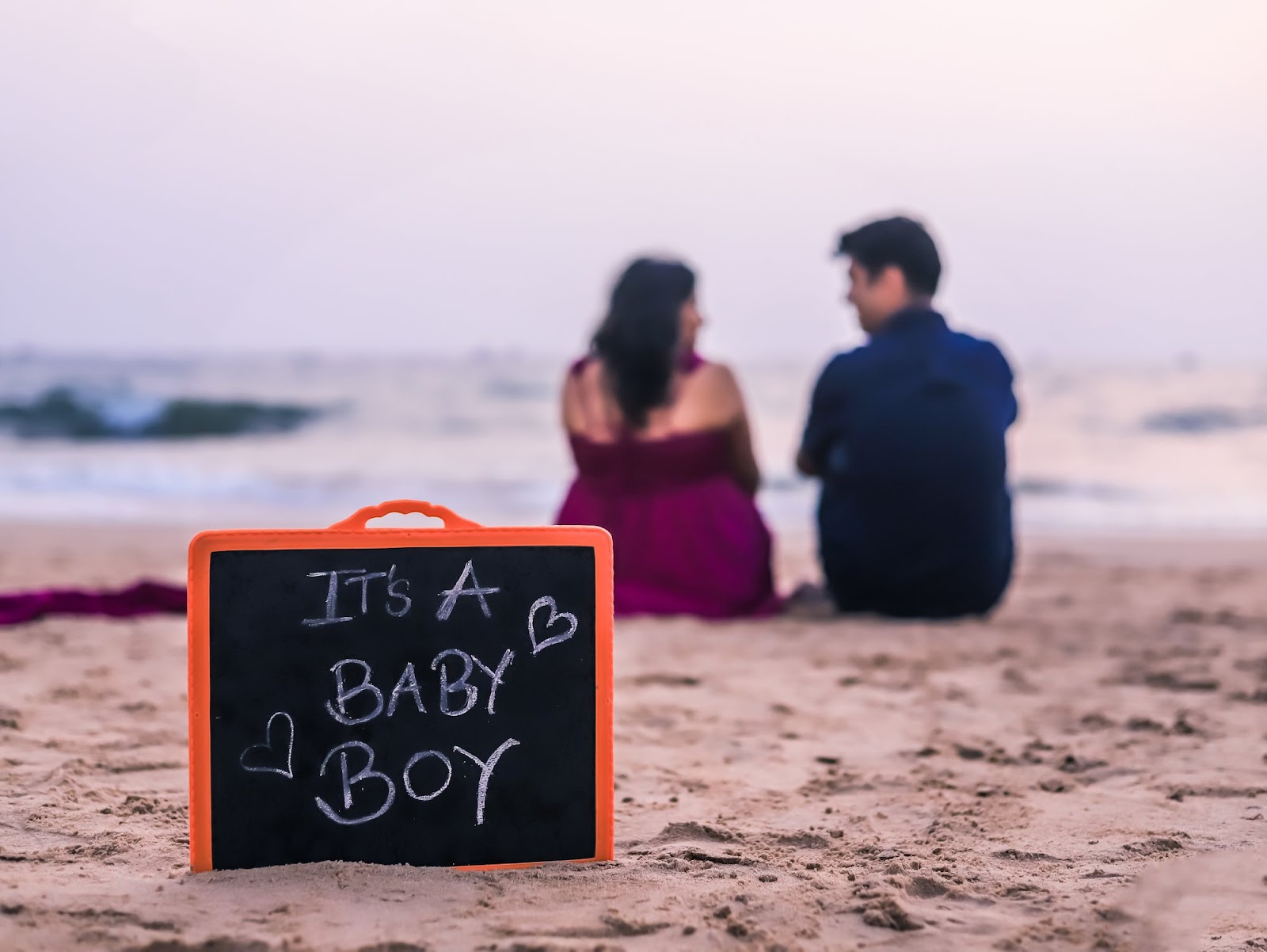 Pregnant couple enjoying a beach maternity photoshoot with a sign revealing their baby boy.