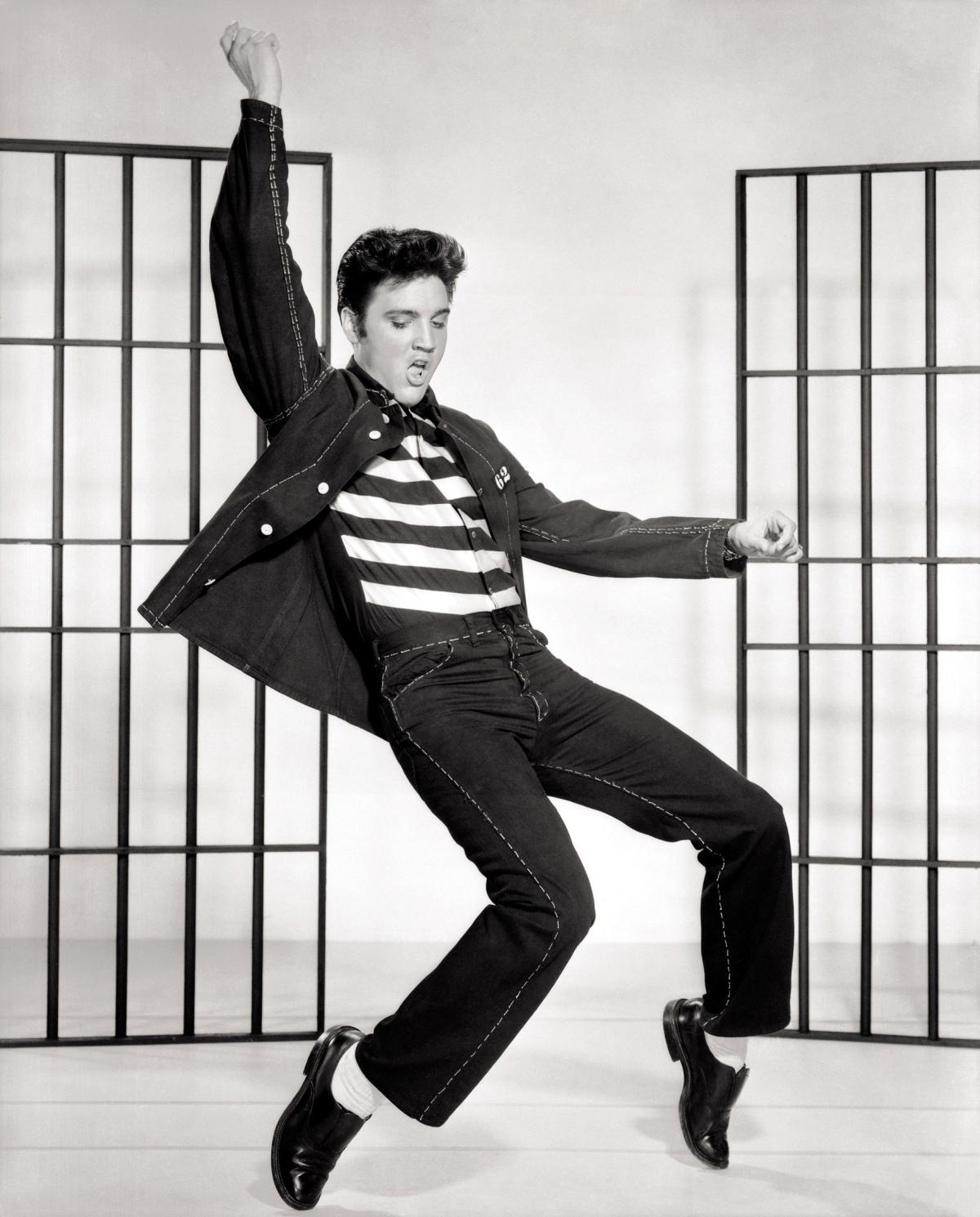 A black and white photo of Elvis Presley, doing one of his signature dance moves.