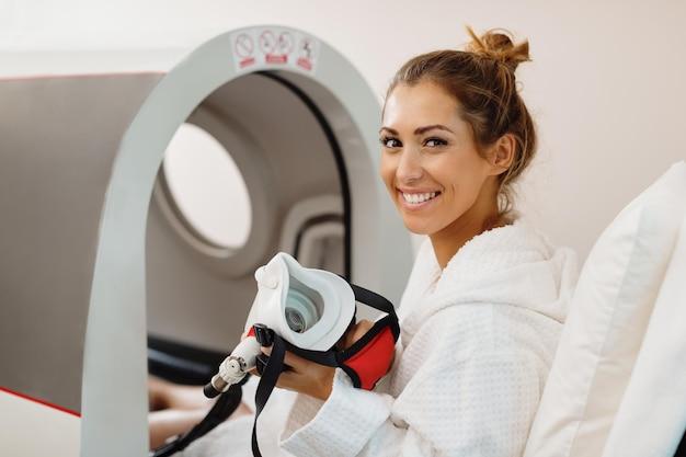 Happy woman having oxygen treatment in hyperbaric chamber at health spa