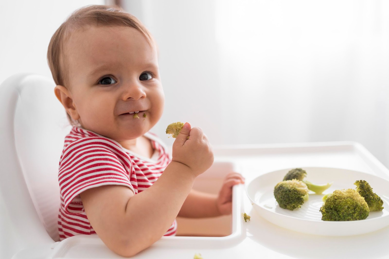 Smiling baby eating vegetables in a high chair