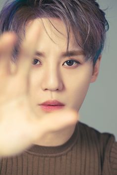 A picture of Junsu wearing a brown shirt stretching his hand forward 