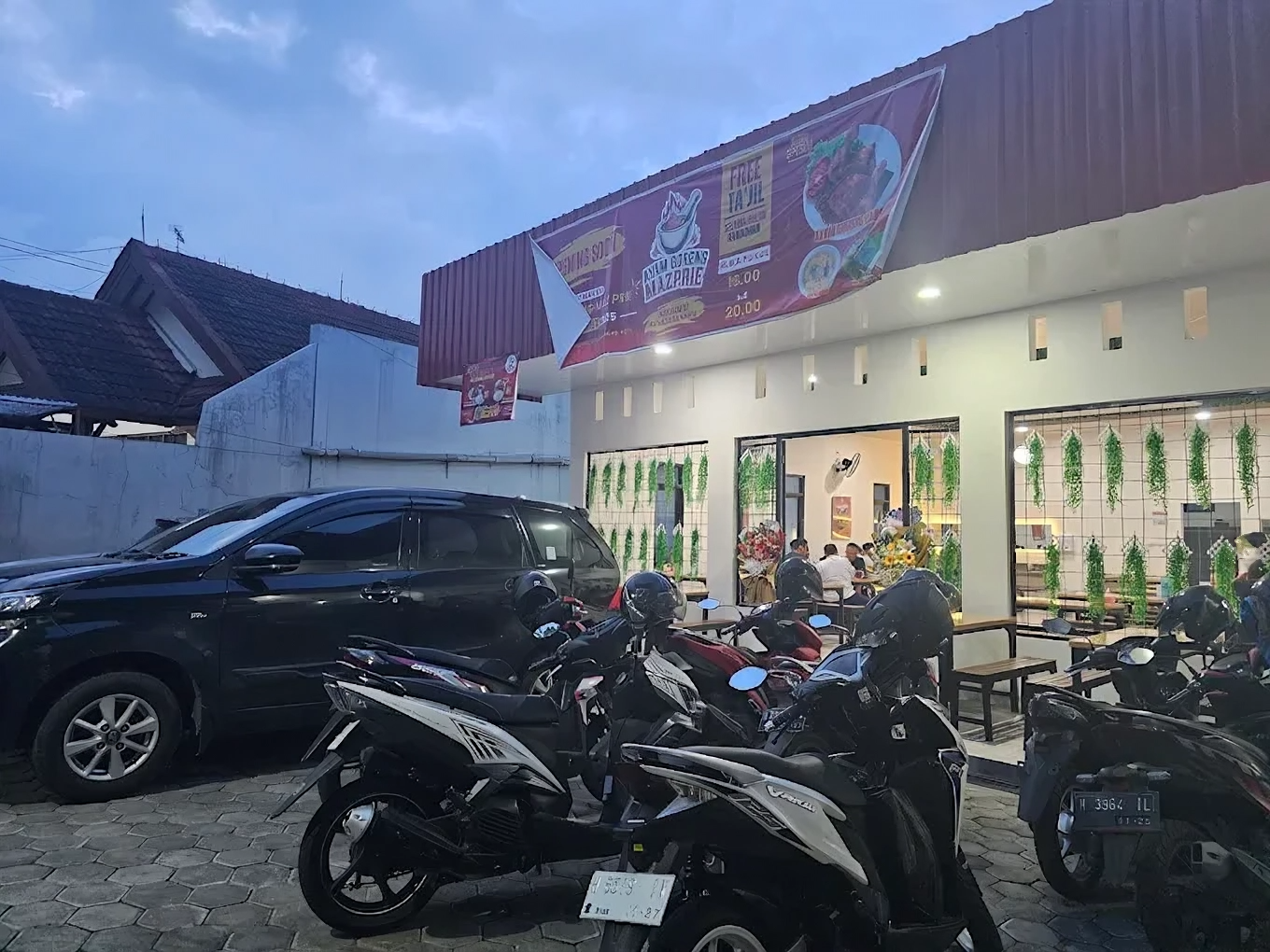 Tampak depan Warung Ayam Goreng Laos Mazprie dengan area parkir penuh motor dan mobil, suasana ramai menjelang malam