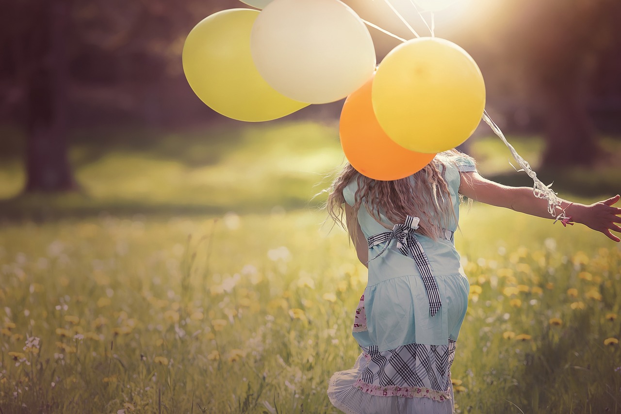 A young girl running with a balloon. Blurred greenery in the background. 