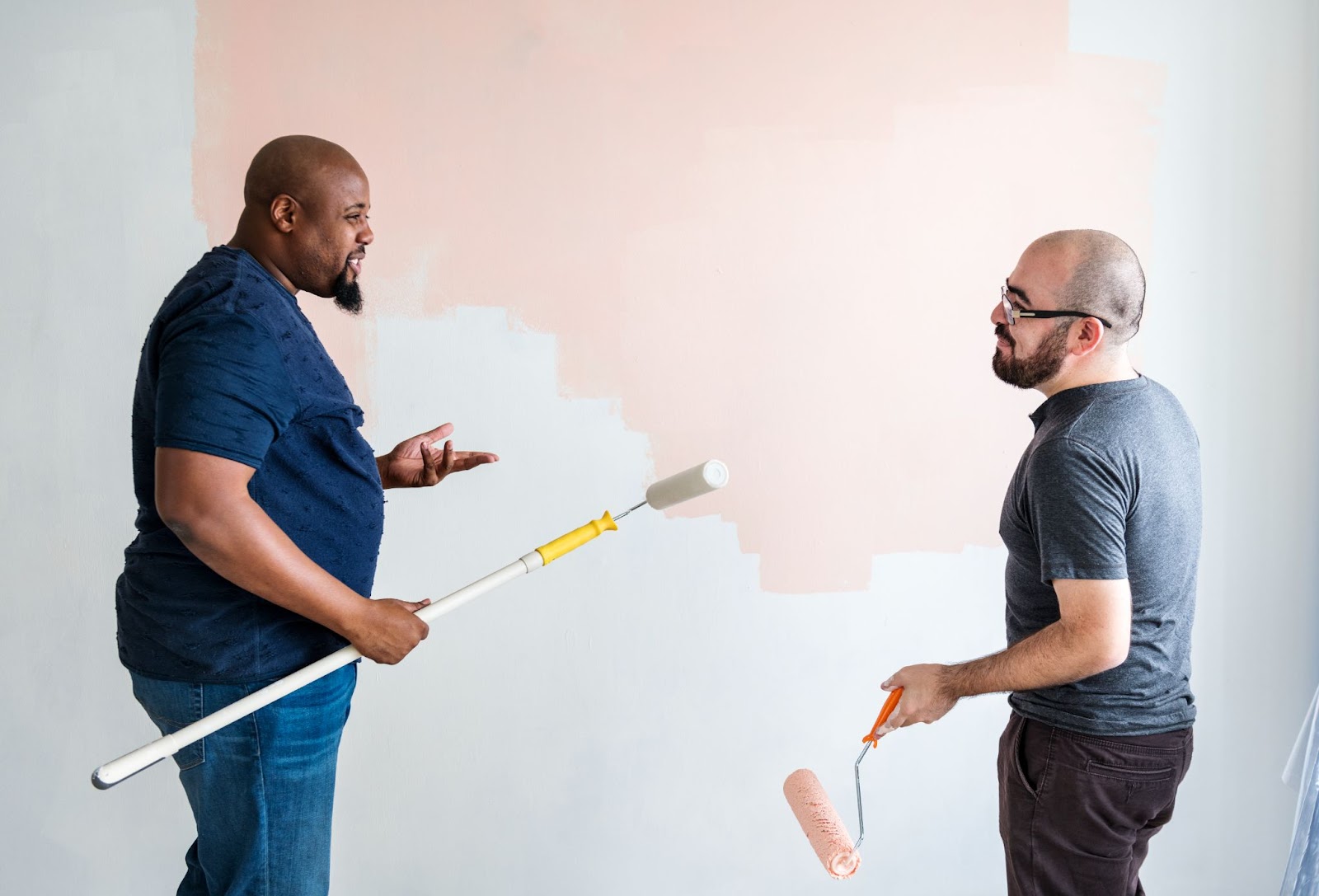 Two men in navy blue shirts discuss the first coat of paint they applied on the wall.