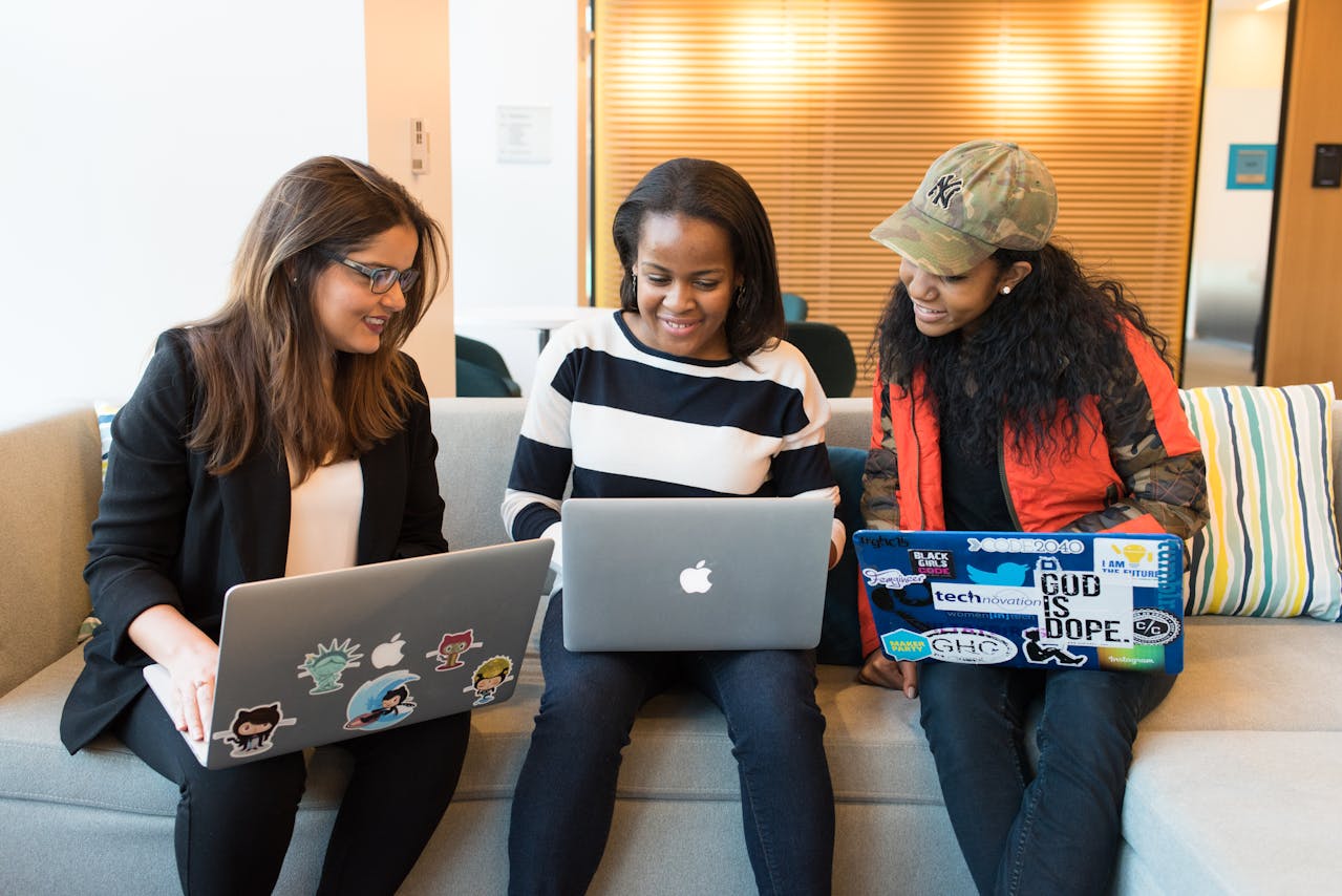 Three women sitting on a couch, each focused on their laptops, creating a cozy and productive atmosphere.