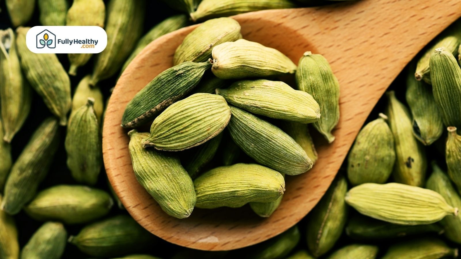 Green cardamom pods in wooden spoon with FullyHealthy logo displayed