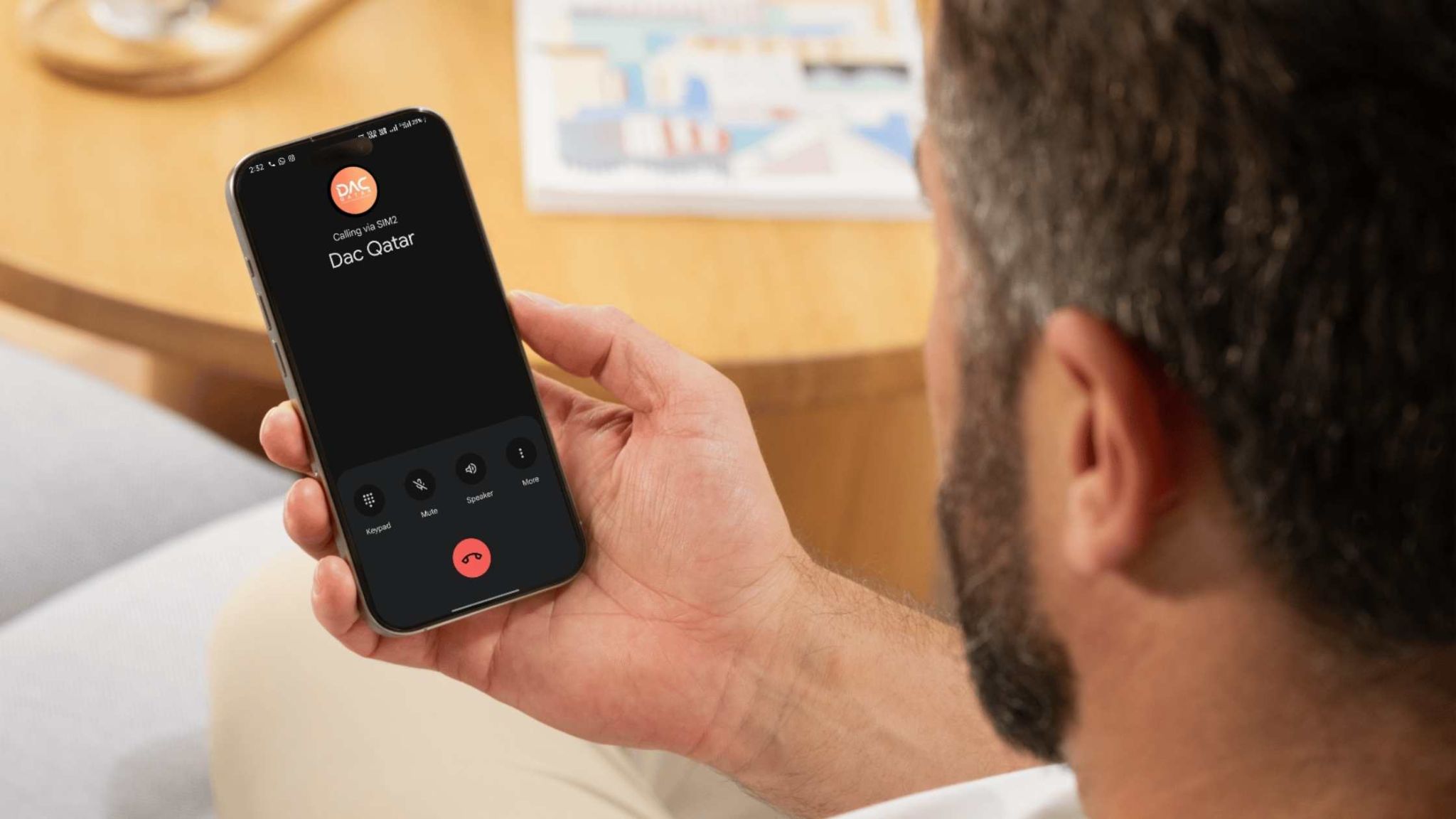 A person holding a smartphone showing an incoming call from "Dac Qatar," with a modern indoor setting in the background – related to Outdoor Digital Display Qatar.