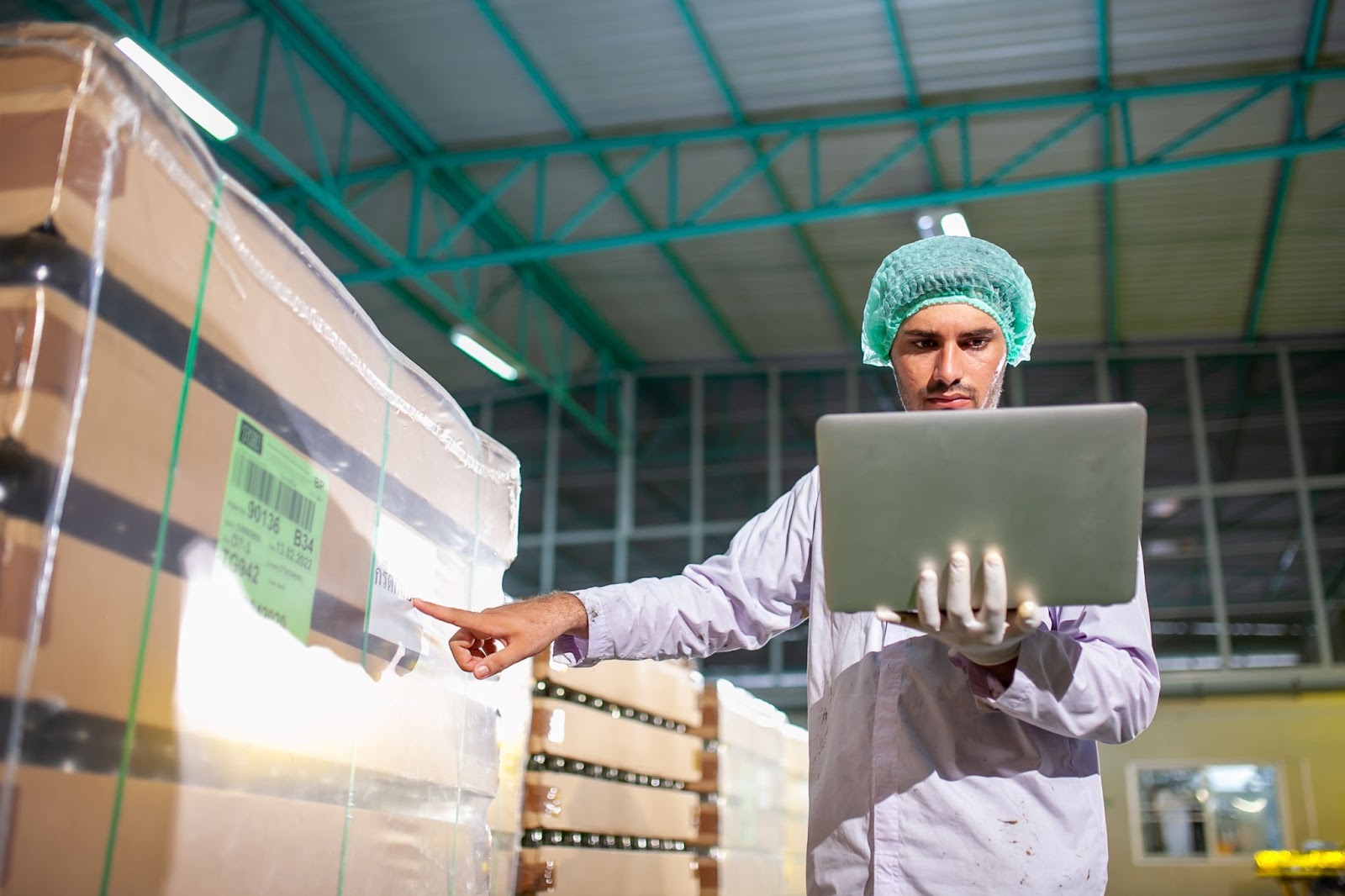 Worker in a hair cap using a laptop to check products on the production line in a beverage factory.